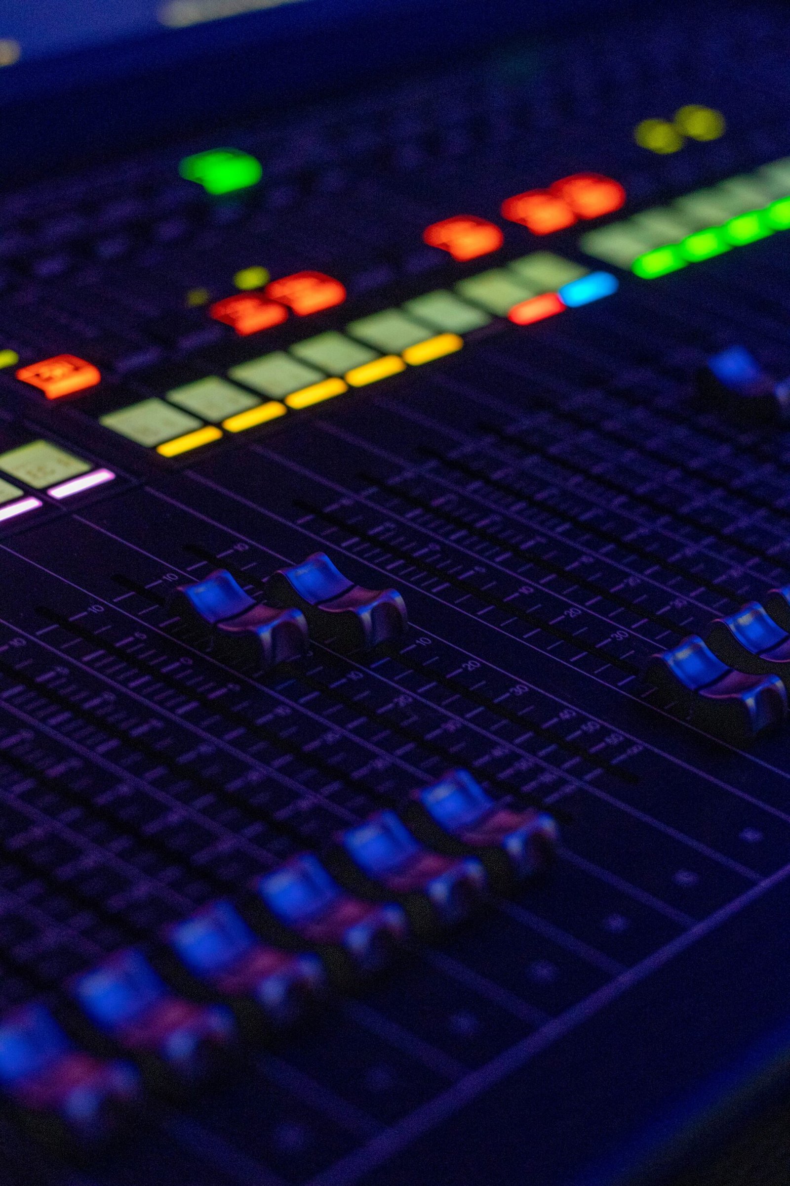 Home A detailed close-up shot of a professional audio mixer with controls and illuminated buttons.